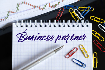 On the desktop are a forex chart, paper clips, a pen and a notebook in which it is written - Business partner