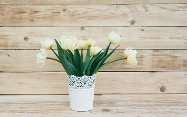 light tulips in a white vase on a wooden background