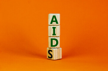 Symbol for helping people with aids, Acquired immunodeficiency syndrome. Turned a wooden cube with words aids aid. Beautiful orange background, copy space. Medical and aids aid concept.