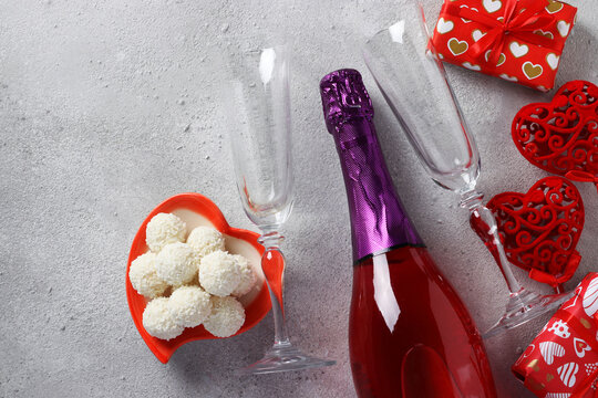 Bottle of champagne, gifts, two glasses and candies on a gray background. Valentine's day concept. Top view