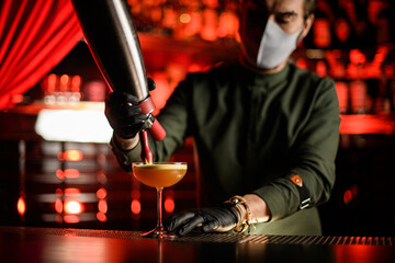 man bartender holds tool in his hands and adds foam to glass with cocktail