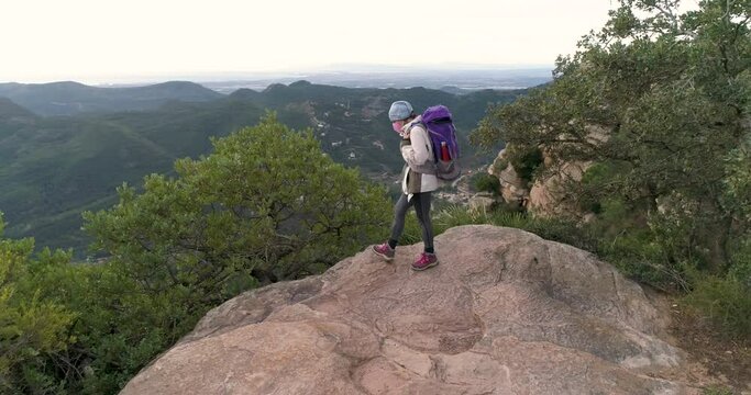 Monta&ntilde;era al borde precipicio con mochila y mascarilla coronavirus mirando horizonte