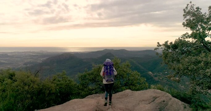 caminante con mochila en la espalda mirando amanecer desde cima monta&ntilde;a