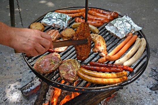 Schwenkgrill mit verschiedenen Fleischwaren Hand wendet Fleisch – Swing grill with various meats hand turns meat