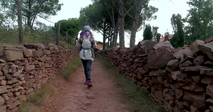 Mujer mediana edad caminando por pasillo de piedras con ropa de invierno y mascarilla covid-19