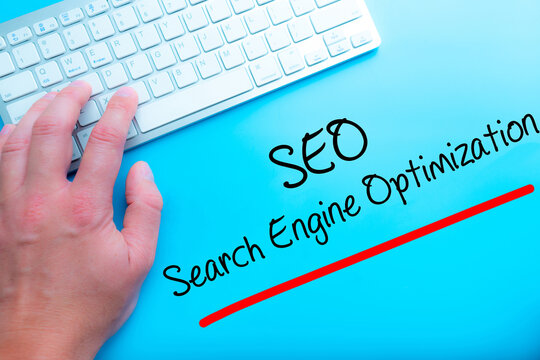 SEO Search Engine Optimization Sign Working at home with computer man writing. Man hands on the keyboard. Isolated on blue background.   Business concept. Stock Photo