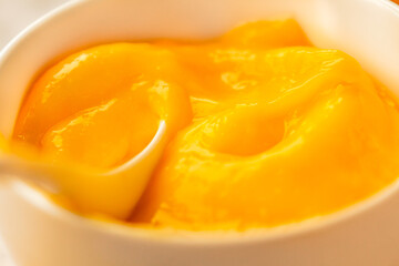 Fototapeta na wymiar Lemon curd in a sausepan white bowl.Close-up yellow smooth background.Horizontal