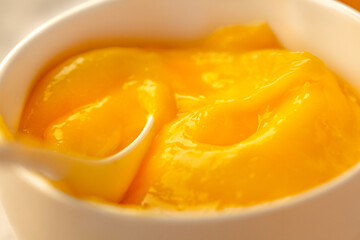 Lemon curd in a sausepan white bowl.Close-up yellow smooth background.Horizontal