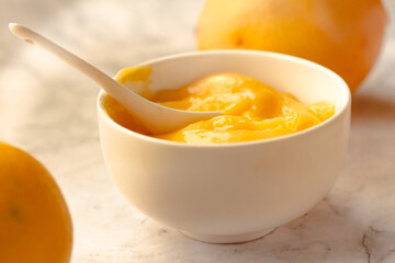 Composition with delicious Yellow lemons and Lemon curd in a sausepan white bowl on marble background