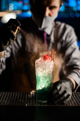 close-up of beautiful glass with blue cocktail that male bartender holds and sprinkles on it