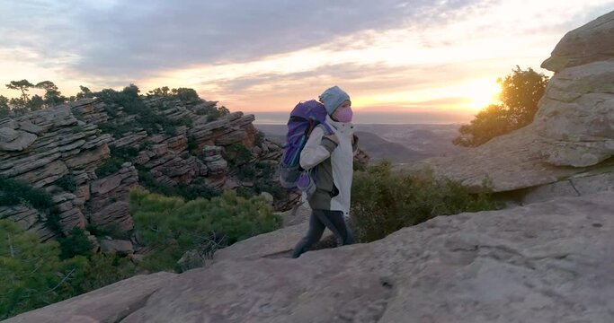 vista lateral de mujer senior escalando al amanecer monta&ntilde;a con mochila