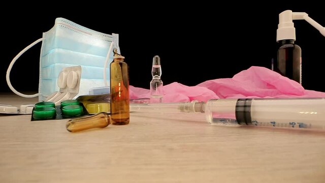 Syringe with vaccine lies near empty ampoule against pills syrup bottle and mask gloves extreme closeup. Concept covid progression