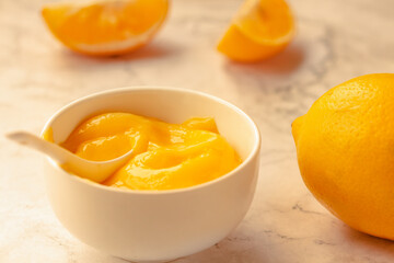 Composition with delicious Yellow lemons and Lemon curd in a sausepan white bowl on marble background