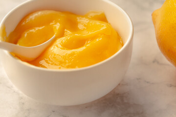 Composition with delicious Yellow lemons and Lemon curd in a sausepan white bowl on marble background