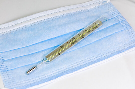 thermometer and medical protective mask close up. medical device for measuring body temperature. thermometer on the background of a medical mask. medical equipment and protection 