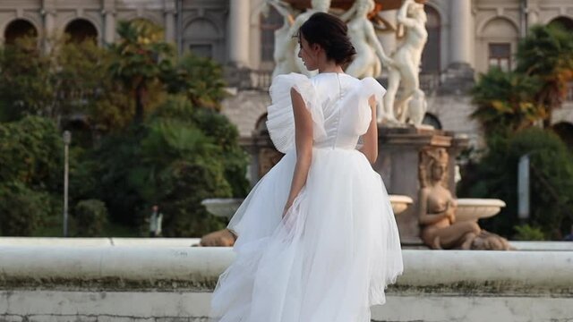 Gorgeous bride run at fountain in park, wearing adorable bridal lace dress. Smiling young woman in wedding dress posing on camera