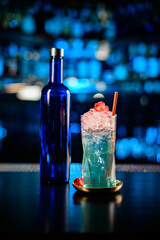 close-up of bottle and glass with cold blue alcoholic cocktail on bar counter