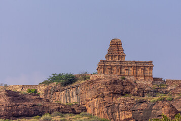 Badami, Karnataka, India - November 7, 2013: Cave temples above Agasthya Lake. Brown stone Upper Shivalaya Temple and wall on reddish rocky hill opposite side of lake under blue sky.