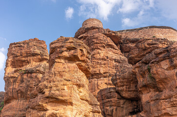 Badami, Karnataka, India - November 7, 2013: Cave temples above Agasthya Lake. Above reddish rock cliffs remnants of fortification with watch tower under blue cloudscape.