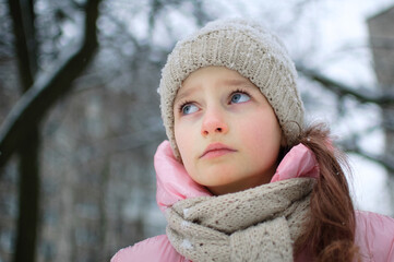 Sad child girl in warm knitted winter clothes spent time outdoors and got frozen.