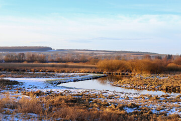 The first snow is a frosty morning. A small river in the grass sprinkled with snow. Golden colors of the morning sun. Rural landscape, Ukraine, Europe.