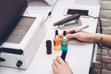 Manicure master table with tools for work. Female hands, nail polish, cuticle oil, brush and electric nail file.