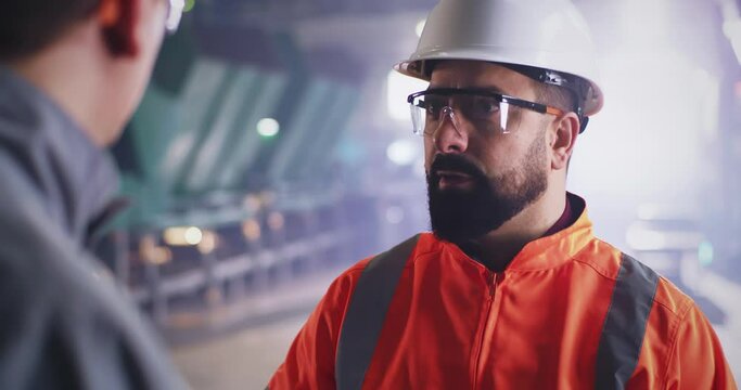 Bearded inspector speaking with worker on factory