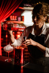 young beautiful woman bartender pours drink from crystal bottle into jigger.
