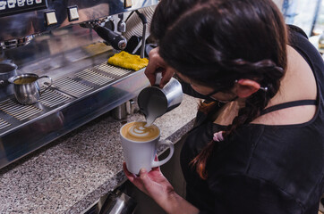 Barista girl preparing a coffee-based drink in a cafeteria, wearing black masks. 4