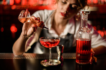 close-up of glass with drink to which woman bartender adds ingredient from small bottle