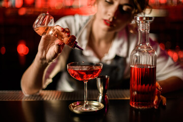 view of glass with drink to which woman bartender adds ingredient from small bottle