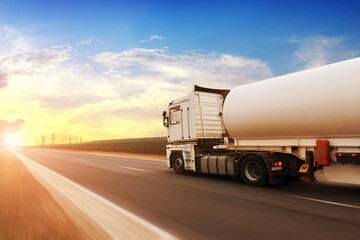 A fuel tanker truck shipping fuel on the countryside road in motion against a sky with a sunset - 411040711