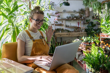Woman gardener wear orange overalls using laptop after work, smiling and talking in video chat, say...