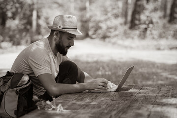 A young man working on laptop outdoors sitting at the wooden antique desk. Concept of travel, freelance, business. Black and white photo.