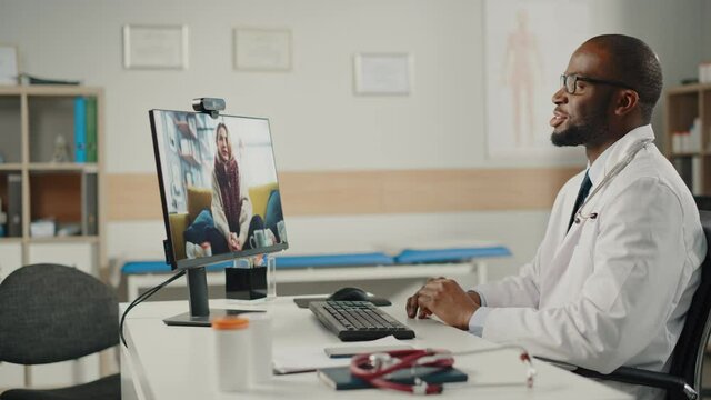 Doctor's Online Medical Consultation: African American Physician Making a Conference Video Call with a Patient on a Desktop Computer
