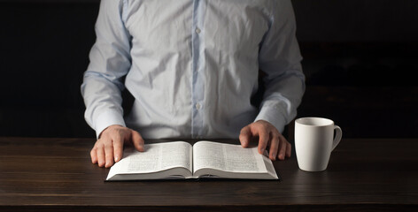 Opened Bible book on a wooden table. Hands of a man in prayer. The concept of love for God's Word.
