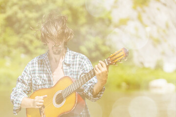 Rock musician man in an open shirt enthusiastically plays the old guitar in nature. Summer, clear...