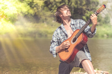 Rock musician man in an open shirt enthusiastically plays the old guitar in nature. Summer, clear...