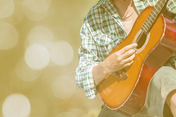 An unrecognizable male musician dressed in a casual style is holding an acoustic wood guitar in...