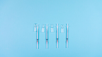 Syringes and ampoules for a vaccine on a light blue background. Concept of medicine, covid vaccination, health protection and life saving. Copy space.