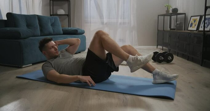 exercise on oblique abdominal muscles, man is training at home at morning, lying on floor and doing crunches, lifting legs
