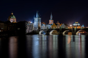 .illuminated Charles Bridge on the Vltava River and light from street lighting is reflected on the surface in the center of Prague at night