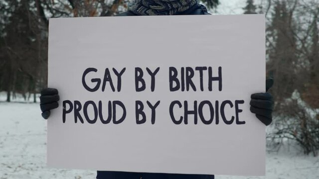 Protesting anonymously in a winter park. An unknown individual with a poster Gay by birth proud by choice claims for the rights of sex minorities. Calling for respect and equality for everybody.