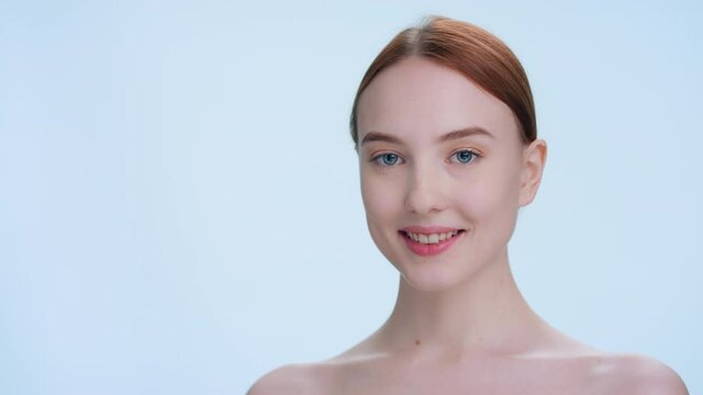Close-up beauty portrait with place for product or sign. Young attractive ginger woman with perfect skin turns, looks at camera and smiles | skin care products commercial concept