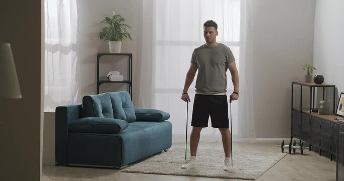 adult handsome man is doing physical exercises with elastic bands at home, strength workout, keeping good physical condition