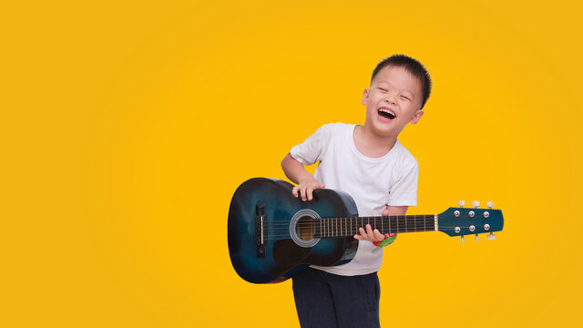 Asian happy smiling boy having fun playing guitar isolated on colored background, Music for kids and toddlers concept
