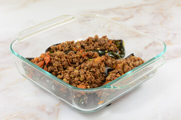 Preparing stuffed poblano peppers in glass baking dish with putting cooked ground beef and tomatoes inside