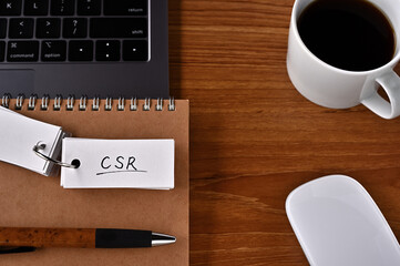 On the desk there is a laptop, a cup of coffee, and a word book with the word CSR written on it. It was an abbreviation for corporate social responsibility.