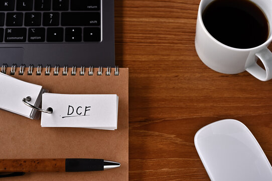 On the desk there is a laptop, a cup of coffee, and a word book with the word DCF written on it. It was an abbreviation for discounted cash flow.