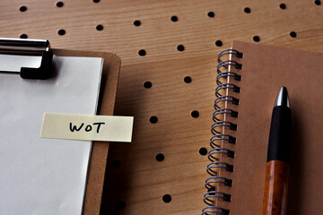 There is a notebook, a pen, and a clipboard with a sticky note stuck to it that says WoT written on...